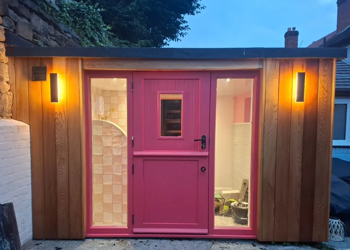Cedar-clad salon conversion with a pink stable door, lit at dusk